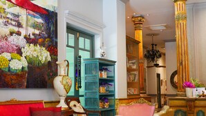 Una habitación con un sofá rojo, un cuadro floral grande, una estantería color turquesa y una columna dorada.