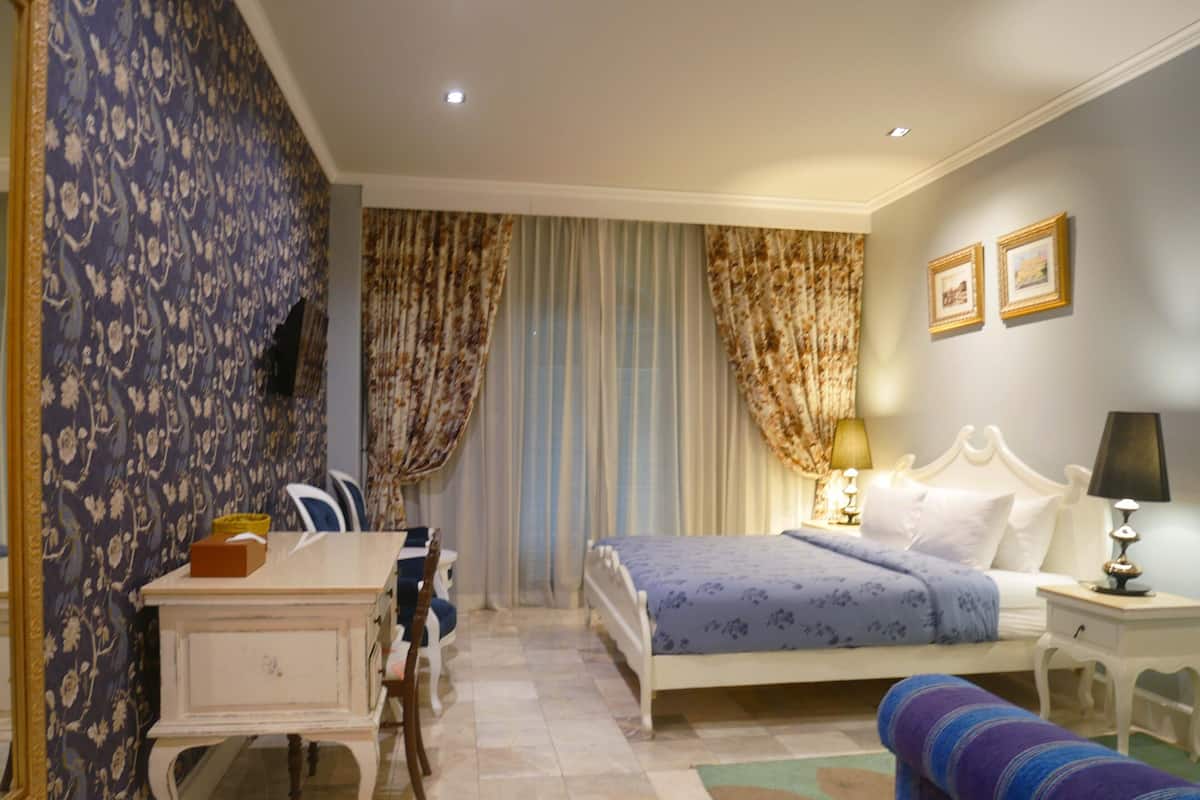 Una habitación de hotel con cama, mesita de noche, lámpara, silla, escritorio y cortinas.