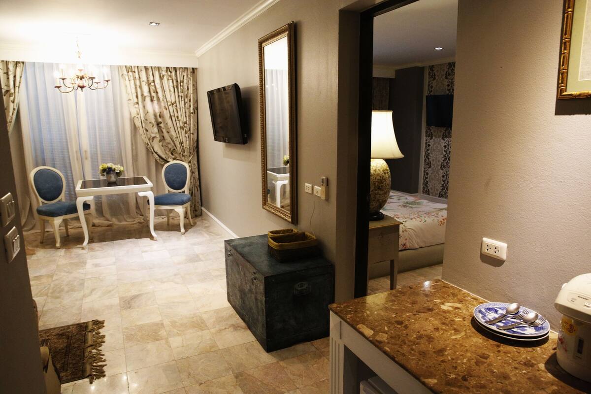Habitación de hotel con comedor, televisor montado en la pared, una pequeña mesa con sillas y una cama con mesita de noche.
