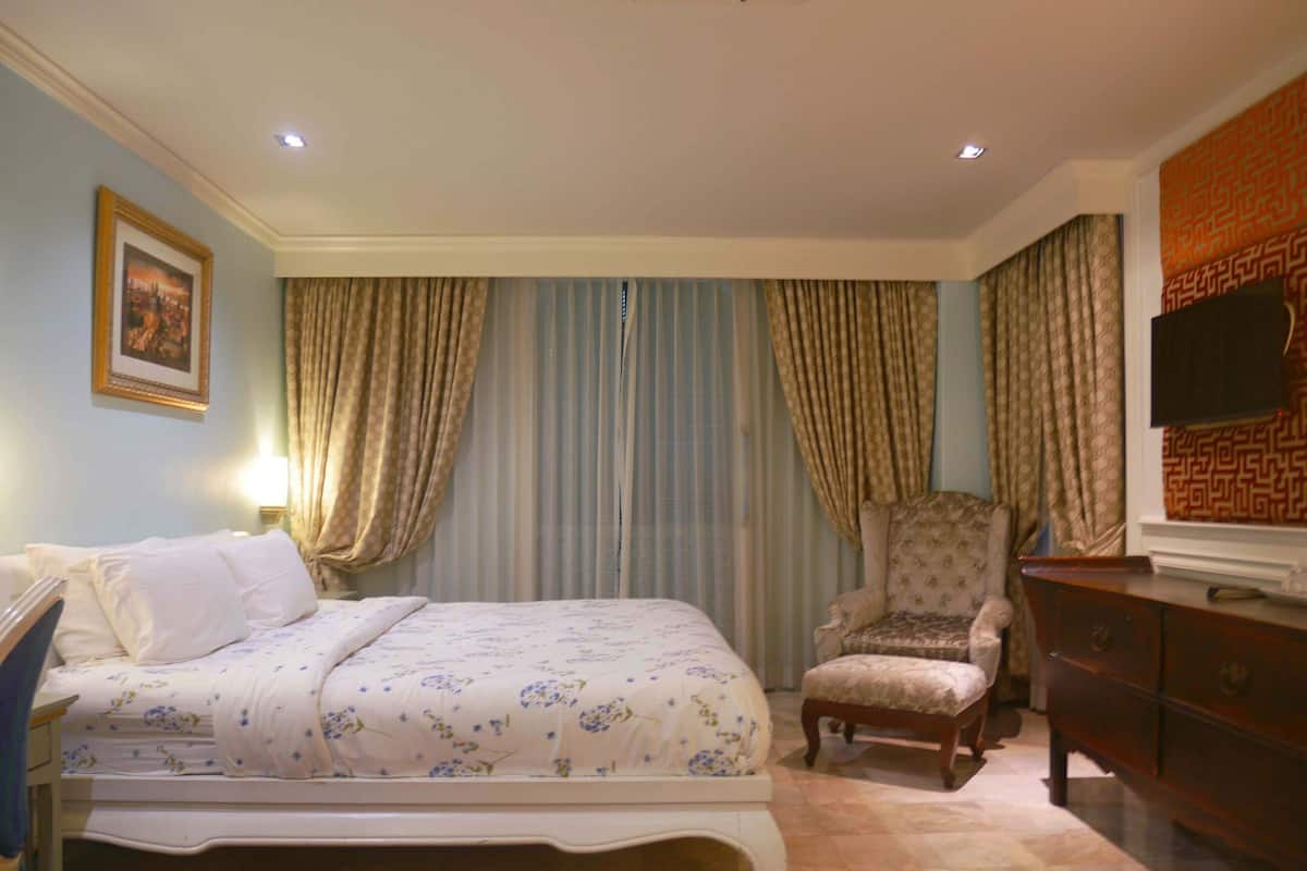 Una habitación de hotel con cama, una silla, cómoda y televisor.