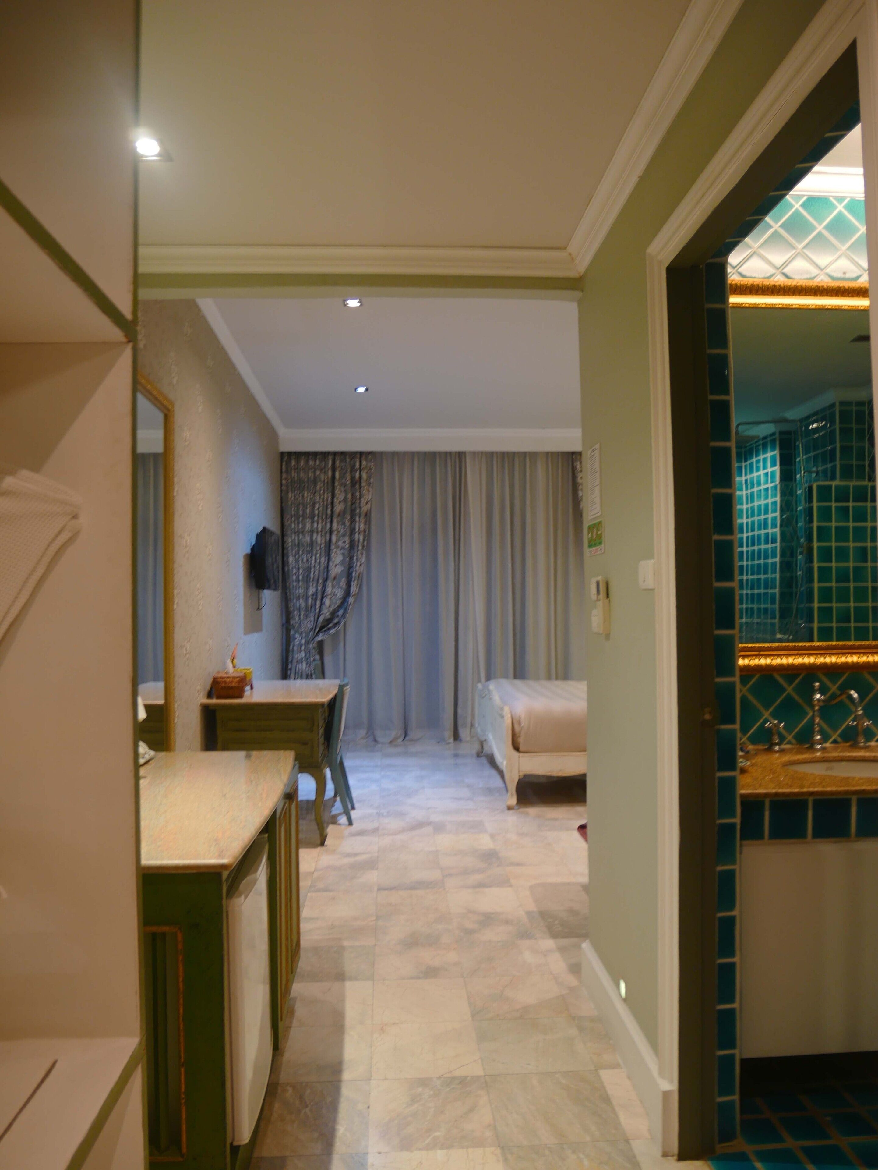 Une chambre d’hôtel comprenant un lit, un bureau, un miroir et une salle de bain avec un mur carrelé.