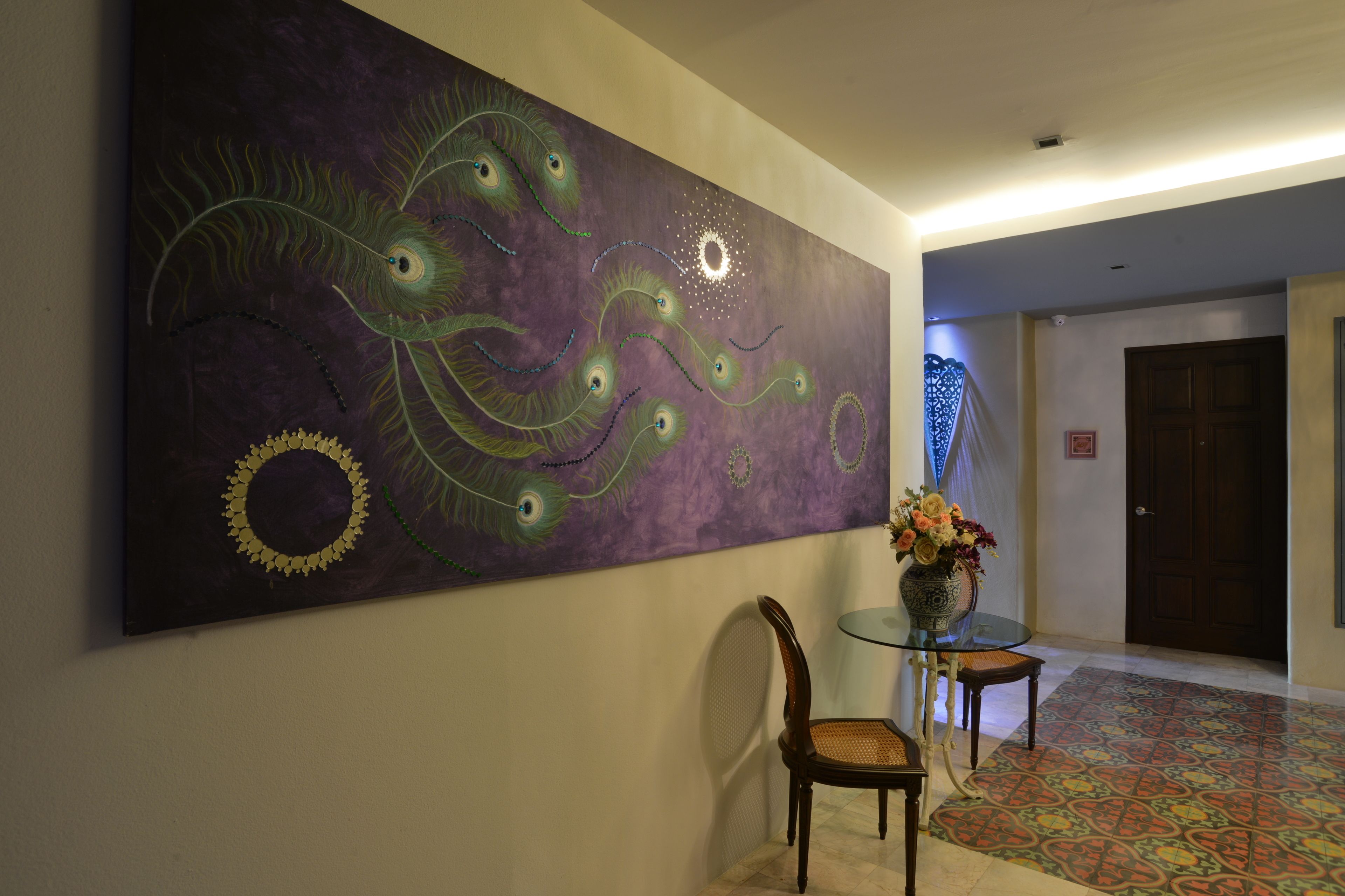 Un pasillo con un cuadro abstracto de gran tamaño, una mesa de vidrio con un florero y un suelo con diseño.