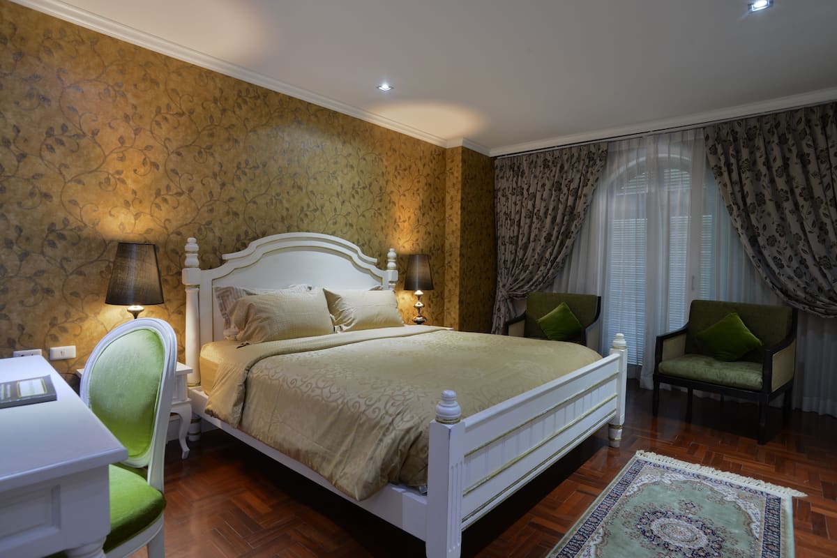 Un dormitorio con cama, dos sillones, escritorio y ventana con cortinas.