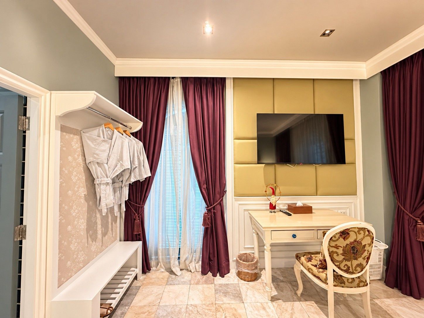 A hotel room with a bed, a desk with a TV, a chair, a piano, and a window with curtains.