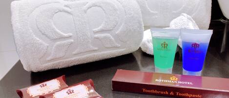 A bathroom with two white towels, a toothbrush, toothpaste, and a bar of soap.