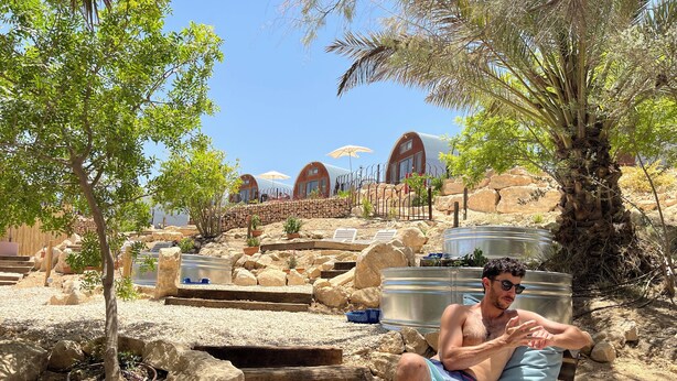 A man relaxing on a wooden deck with a pool and palm trees in the background.