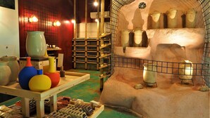 A room with a rustic stone wall, shelves with bottles, and a display of colorful vases.