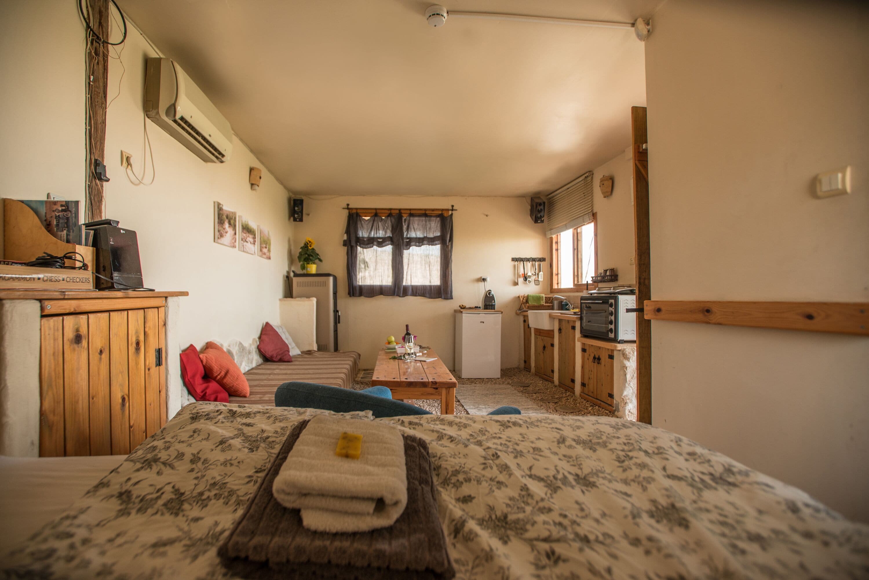 A cozy room with a bed, a small desk, a kitchenette, and a window with curtains.