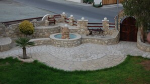 A stone courtyard with a fountain, benches, and a wooden gate. - Moniatis Hotel (Limassol)