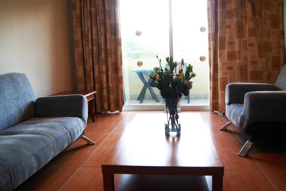 A living room with a sofa, armchair, and a coffee table with a vase of flowers.