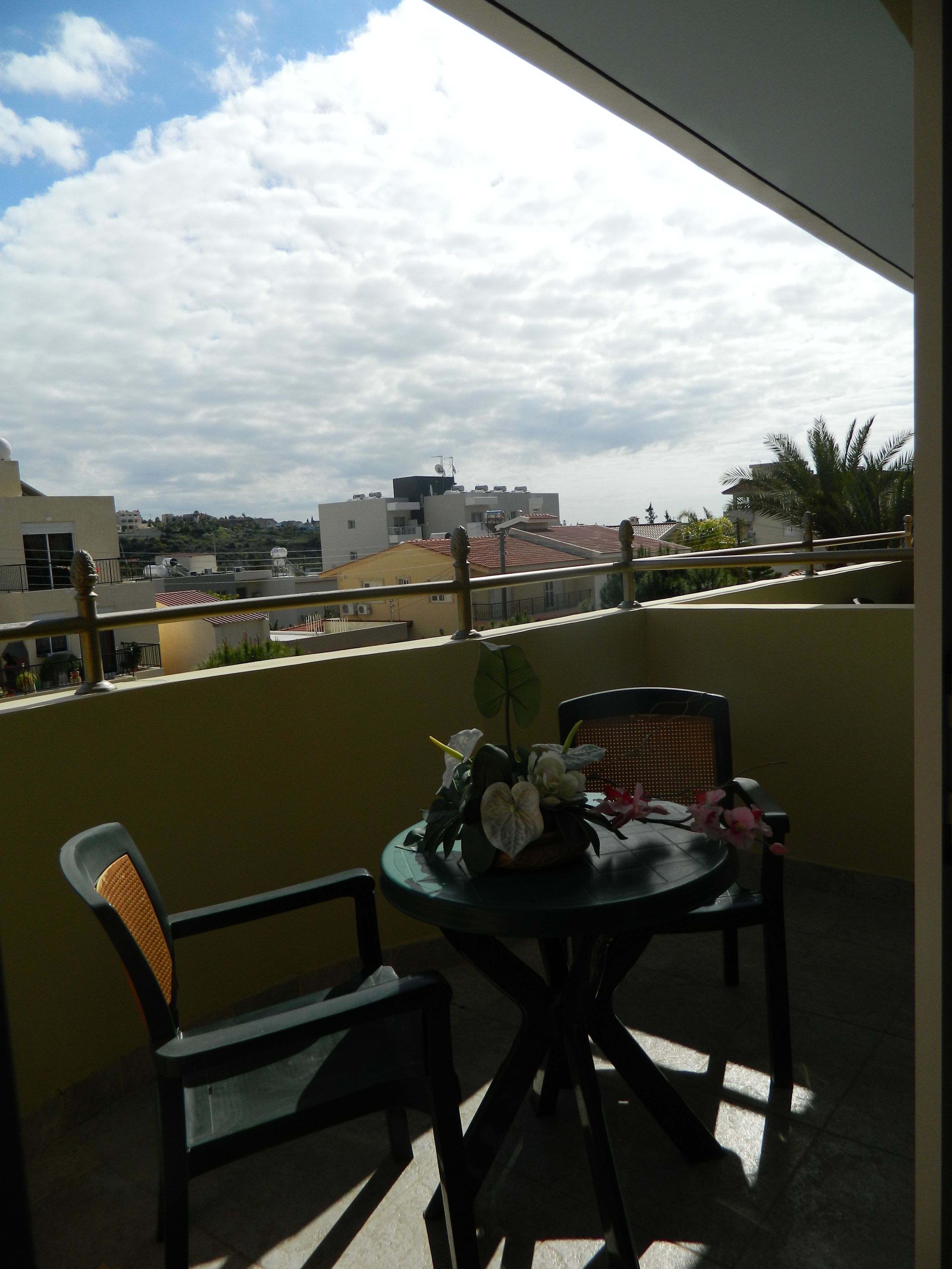 A balcony with a table and chairs, a view of the cityscape, and a partly cloudy sky.