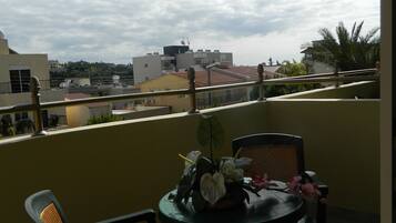 A balcony with a table and chairs, a view of the cityscape, and a partly cloudy sky.