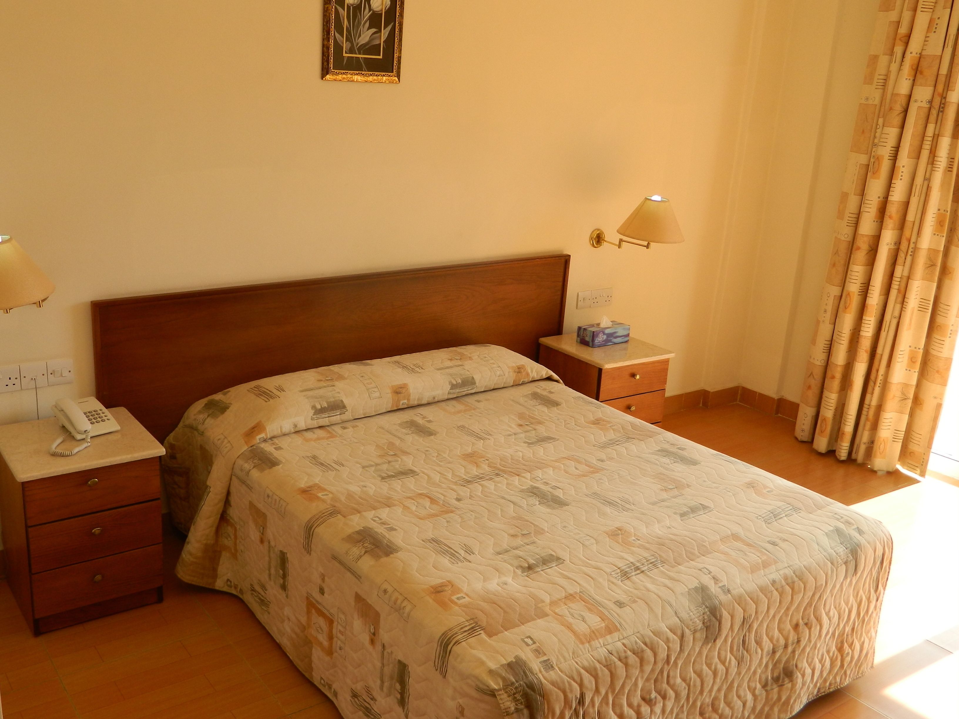 A hotel room with a wooden bed, a bedside table with a lamp, a phone, and a nightstand with a tissue box.
