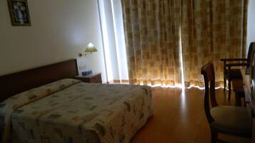 A hotel room with a bed, a desk, a chair, a lamp, and a window with curtains.