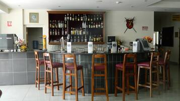 A bar area with a tiled floor, wooden bar stools, a counter with a cash register, and a wall-mounted liquor display.