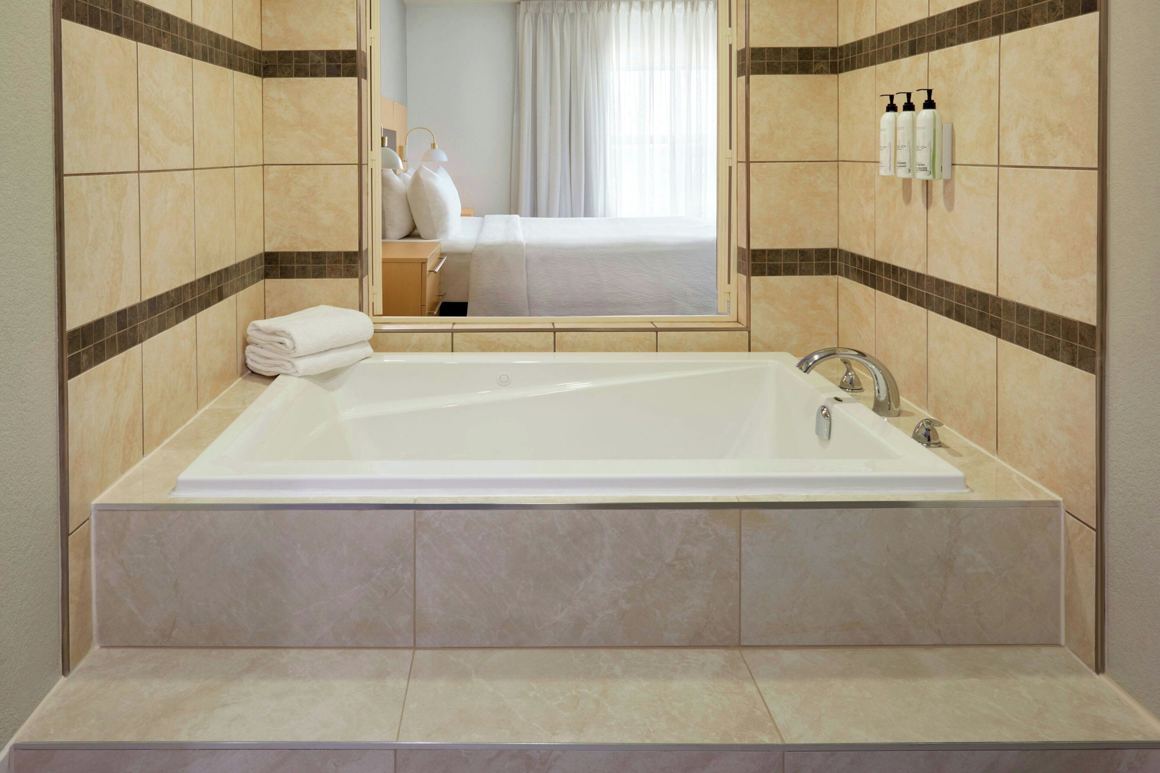 Une salle de bain moderne avec une grande baignoire, un miroir et une fenêtre.