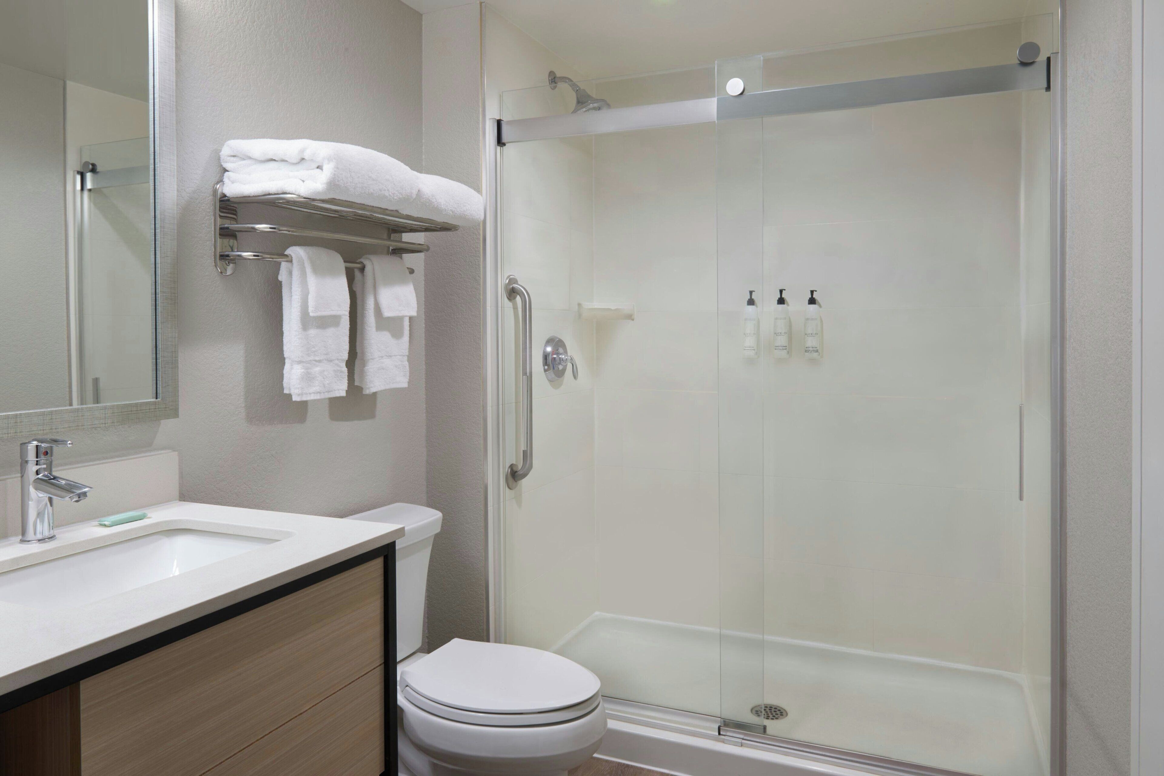 A modern bathroom with a glass-enclosed shower, a white toilet, a sink with a mirror, and a towel rack with folded towels.