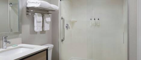 A modern bathroom with a glass-enclosed shower, a white toilet, a sink with a mirror, and a towel rack with folded towels.