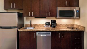 A compact kitchen with dark brown cabinets, a stainless steel refrigerator, a microwave, a coffee maker, and a dishwasher.