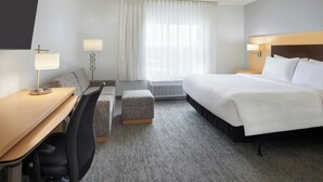 A hotel room with a bed, a desk, a chair, a small ottoman, and a window with curtains.