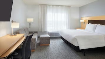 A hotel room with a bed, a desk, a chair, a small ottoman, and a window with curtains.