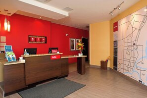 Un hall d’accueil d’hôtel avec un mur rouge, un comptoir d’accueil en bois et une carte affichée au mur.