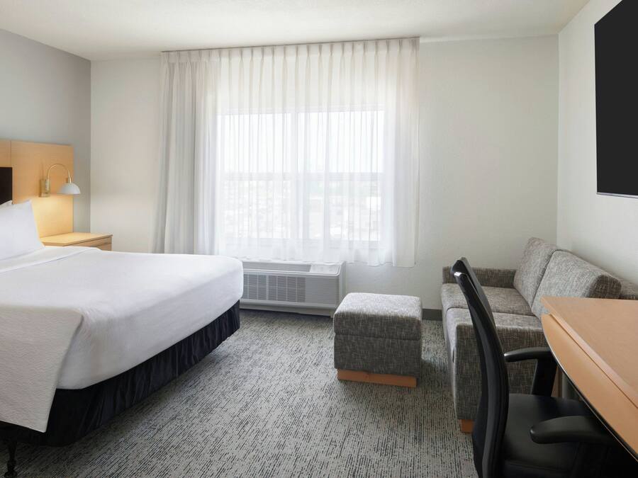 Habitación de hotel con cama, escritorio, silla, calefactor y ventana con cortinas.