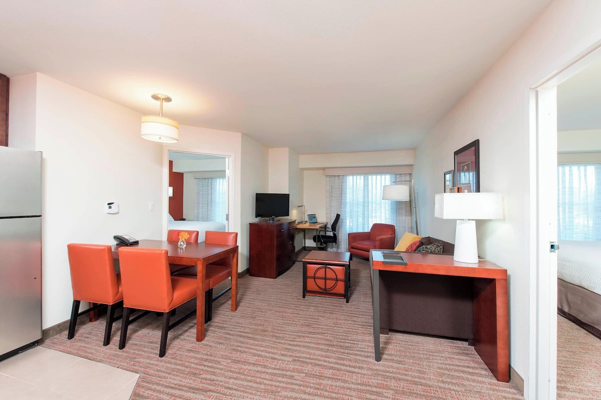A hotel room with a dining area, a desk with a lamp, a TV, and a bed.