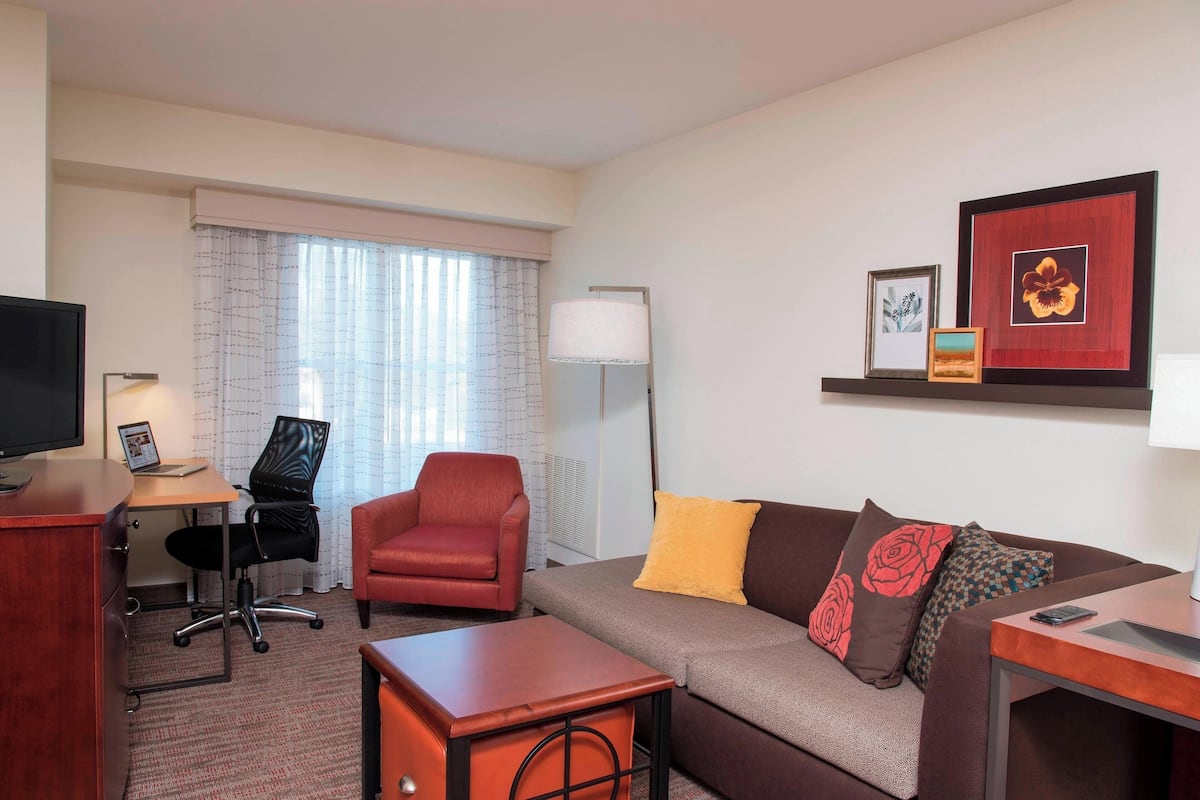 A hotel room with a sofa, armchair, desk, and a TV.