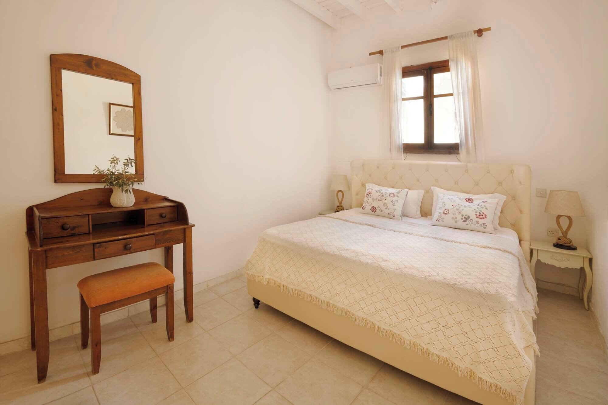 A bedroom with a bed, a nightstand, a dresser, a mirror, and a window with curtains.