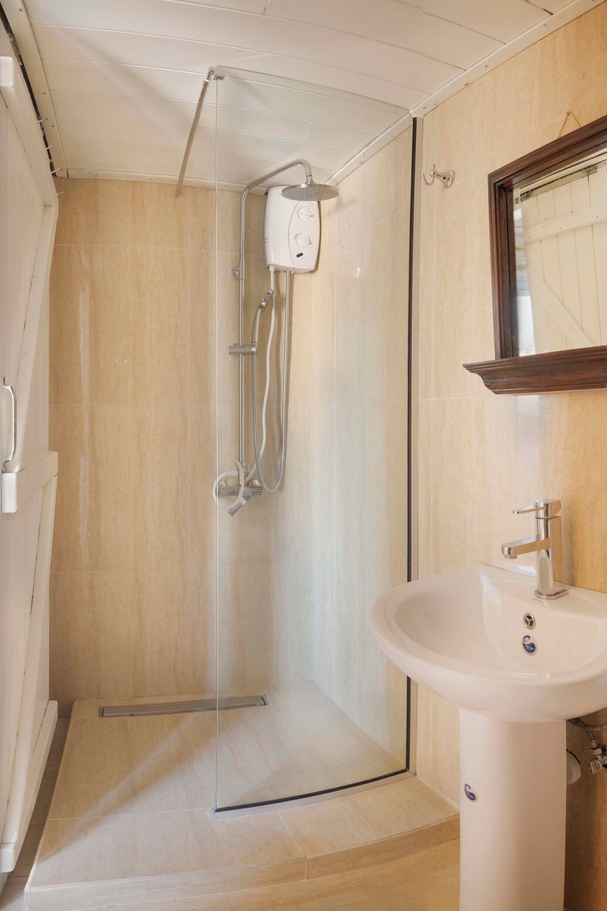 Une salle de bain avec une douche à parois de verre, un lavabo blanc et un miroir encadré en bois.