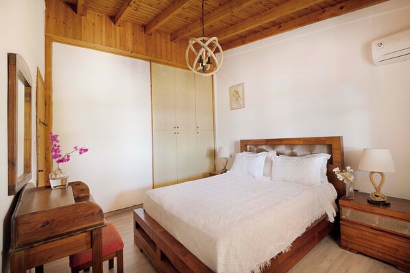 A bedroom with a wooden bed, a nightstand with a lamp, a wooden desk, and a chair.