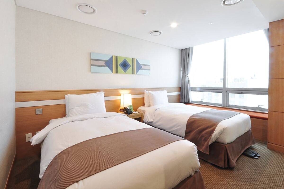 Habitación de hotel con dos camas, un ventanal grande y una obra de arte colgada en la pared.