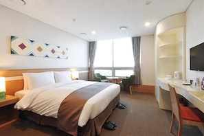 A hotel room with a bed, desk, chair, TV, and a window with curtains.