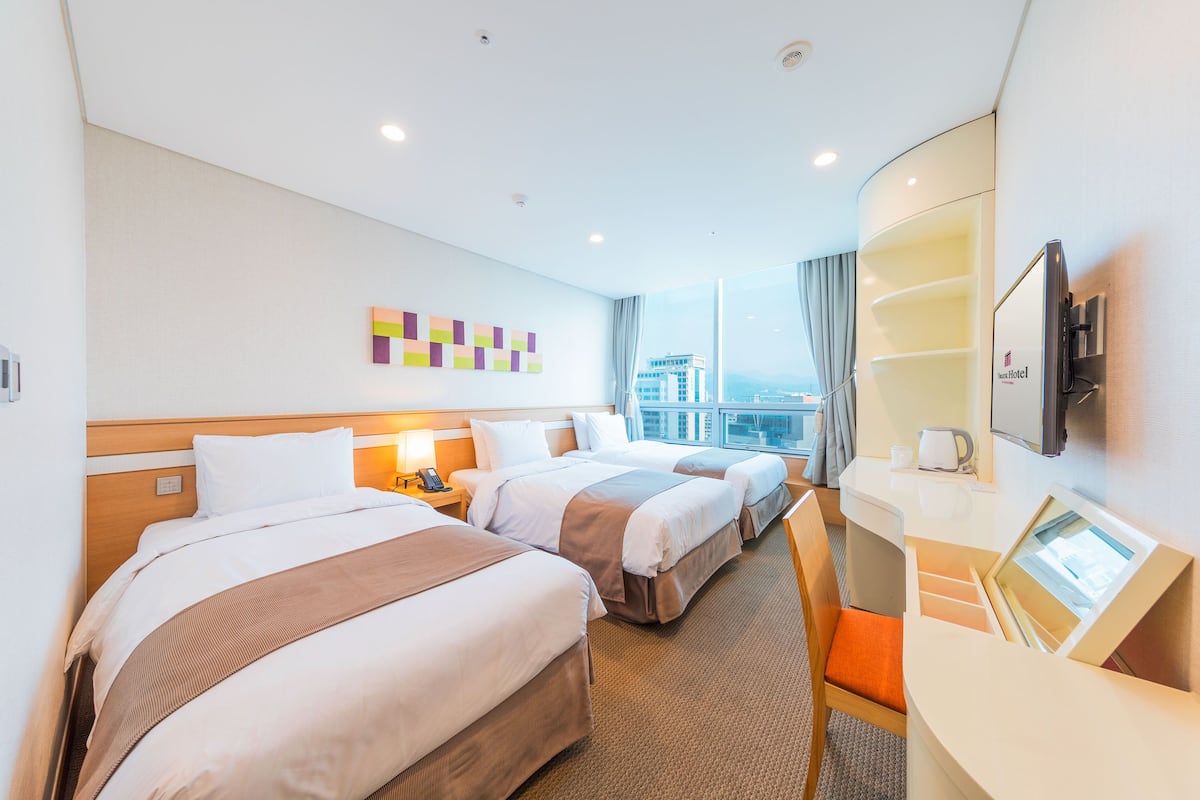 Habitación de hotel con dos camas, un escritorio, un televisor y una ventana con vistas a la ciudad.