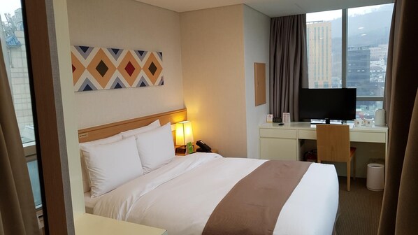 Habitación de hotel con cama, escritorio con computadora, silla, televisor y ventana con vista a la ciudad.
