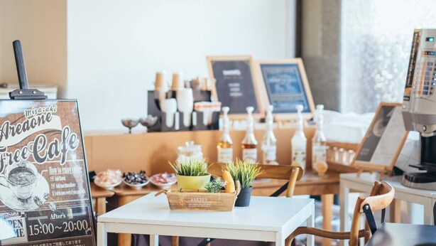 Interior de una cafetería con una pizarra de menú, máquina de café y una exhibición de plantas.