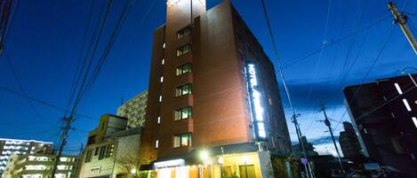 Un hotel de varios pisos con un cartel llamativo, una entrada bien iluminada y un estacionamiento visible en primer plano.