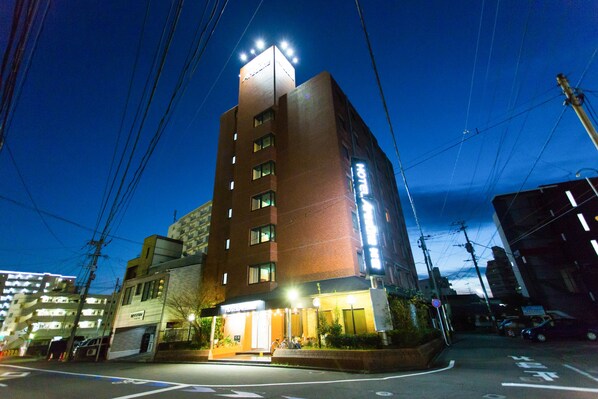 A multi-story hotel with a prominent sign, a well-lit entrance, and a parking area visible in the foreground.