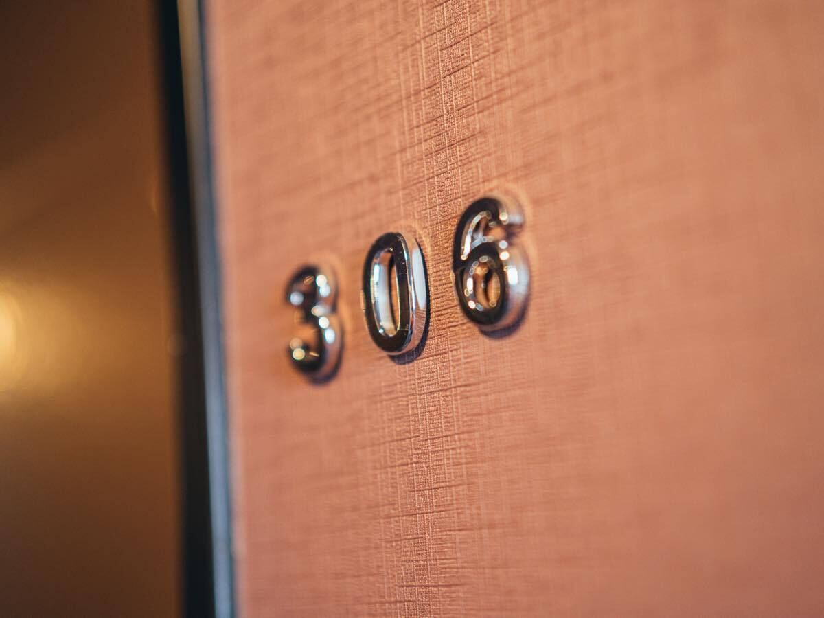 Primer plano de una pared texturizada con el número "306" en relieve, hecho con un material reflectante.