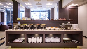 Un'area buffet con diverse postazioni per il cibo e posate, una macchina per il caffè e un angolo relax con divano e sedie.