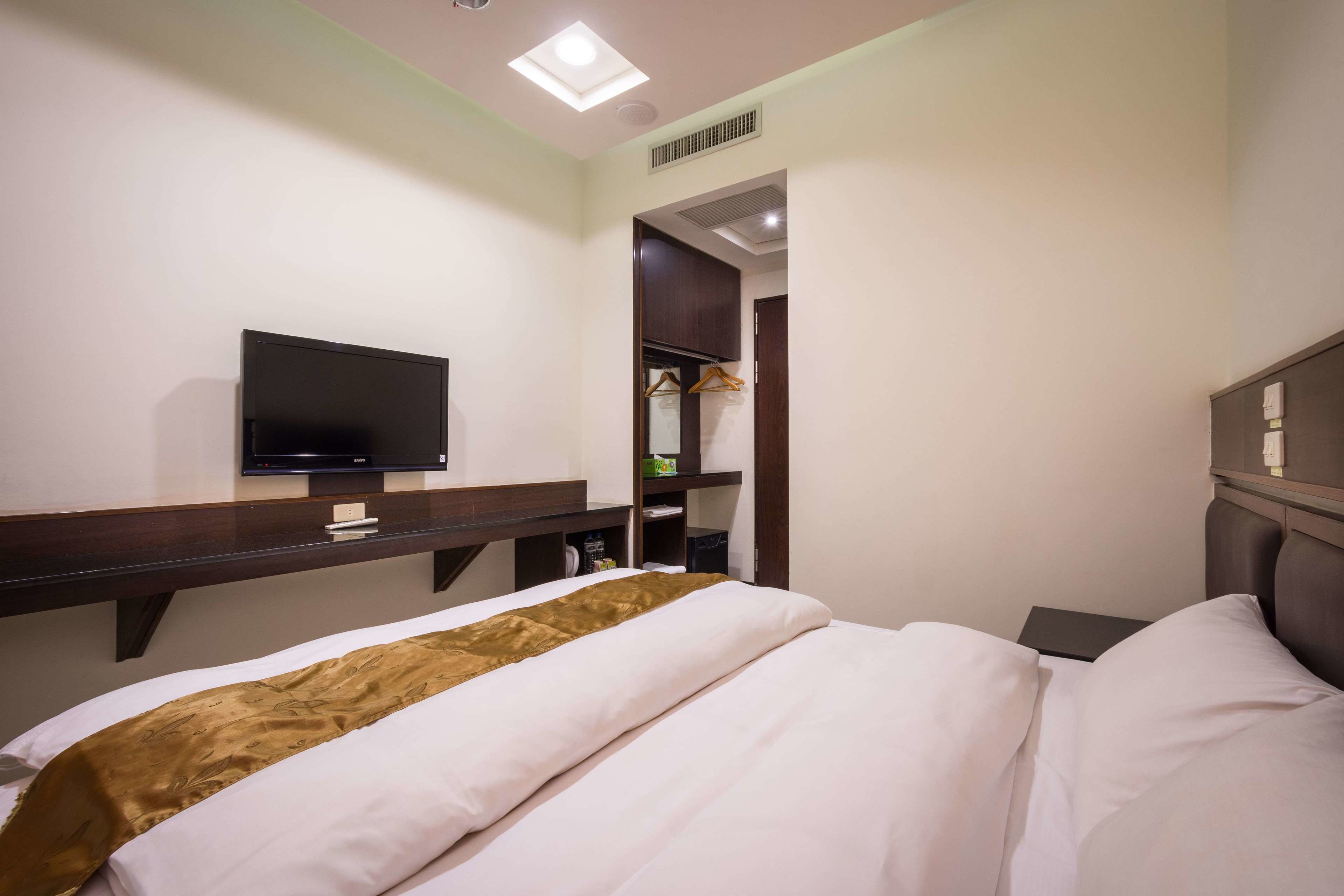 Habitación de hotel con cama, televisor montado en un estante de madera, armario y una mesita.