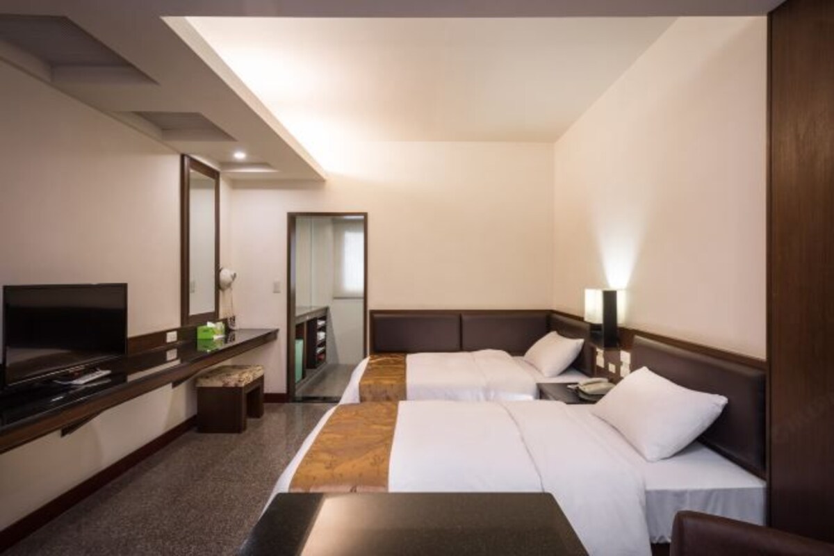 Una habitación de hotel con dos camas, televisión, escritorio y espejo.