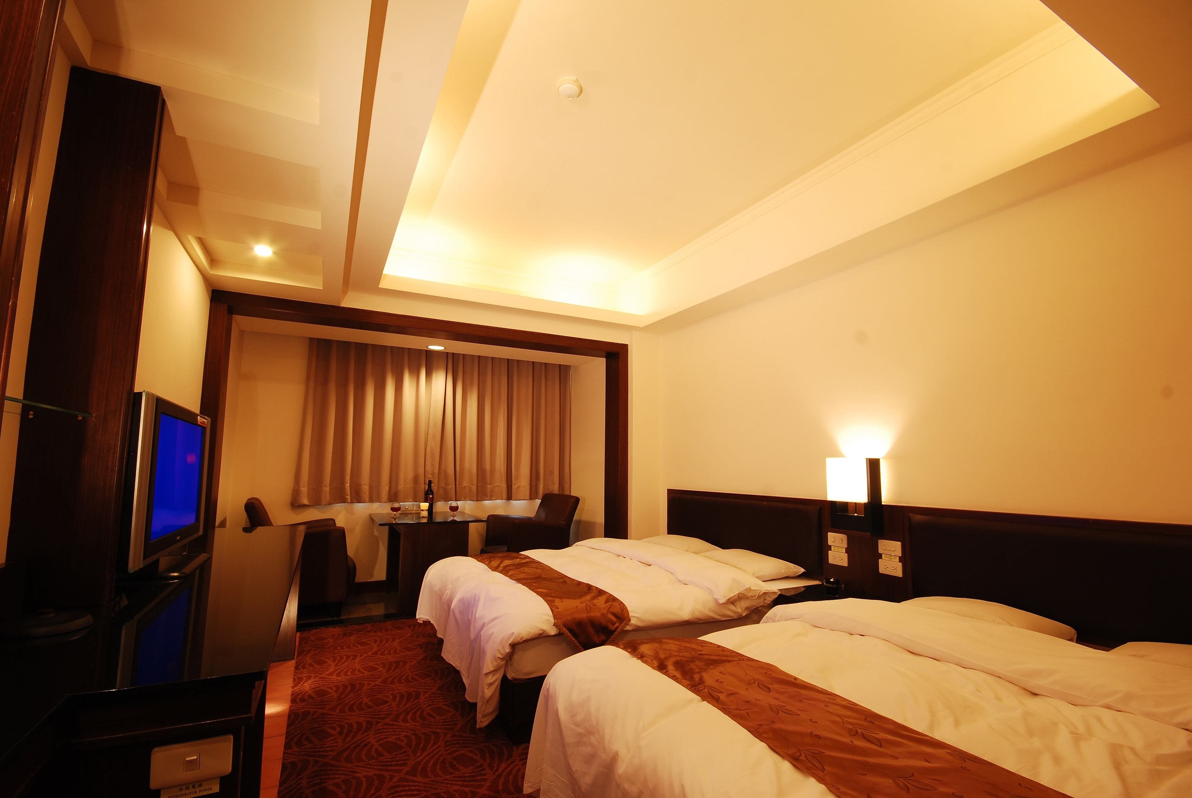 A hotel room with two beds, a desk with a computer, a TV, and a window with curtains.