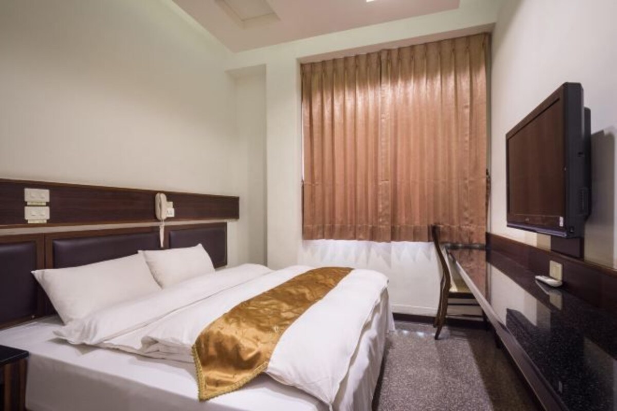 Una habitación de hotel con cama, televisión, escritorio y ventana con cortinas.