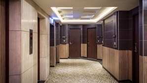 Un corridoio moderno di un hotel con pannelli in legno, una moquette decorata e un soffitto con luci a incasso.