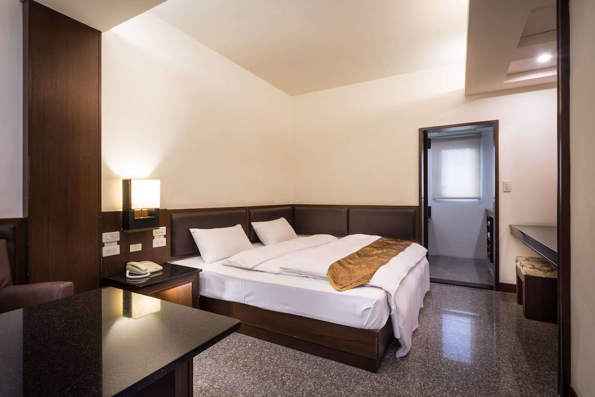 A hotel room with a bed, bedside table, lamp, and a door leading to a bathroom.