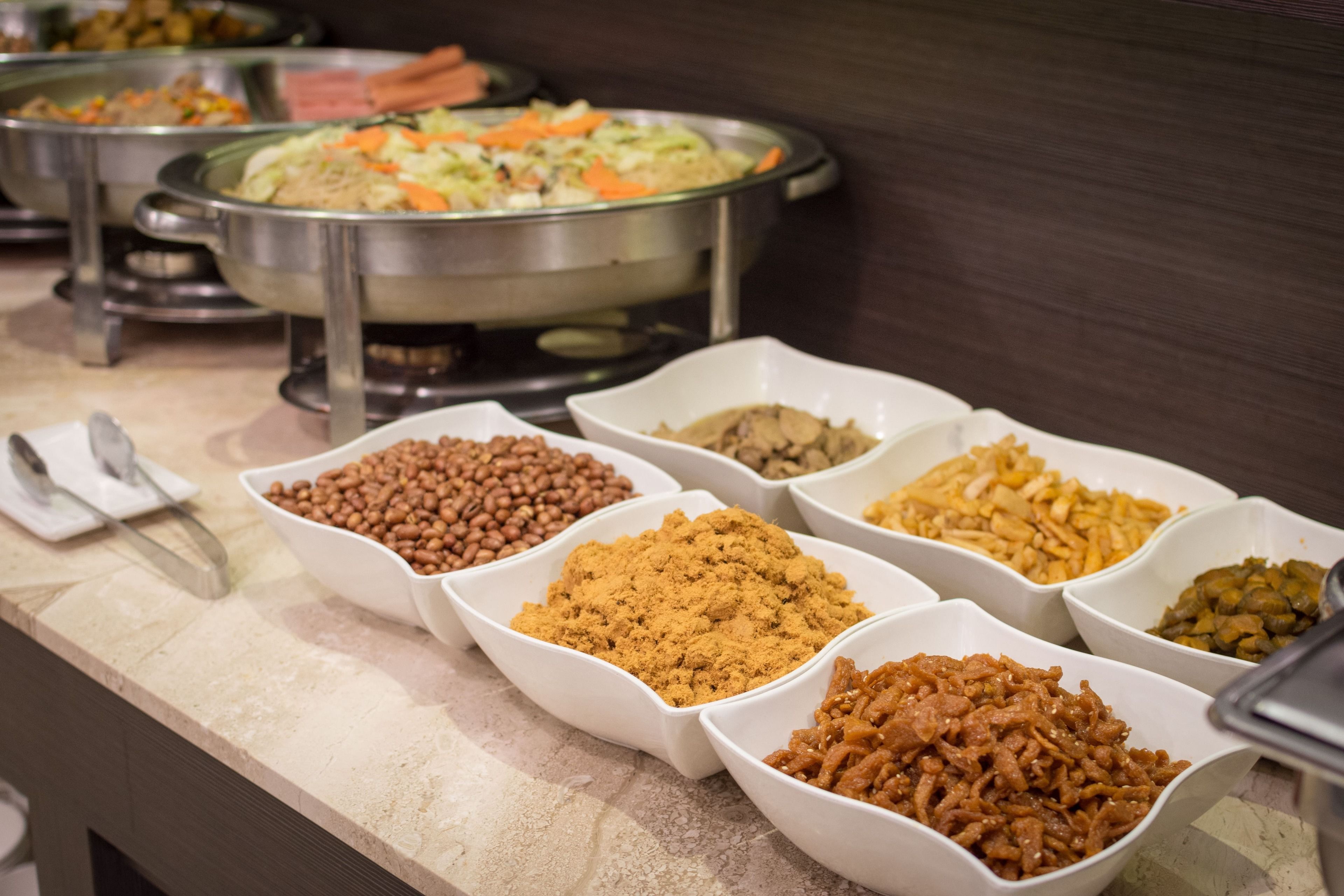 A buffet with various food items in white bowls, including beans, nuts, and other snacks.