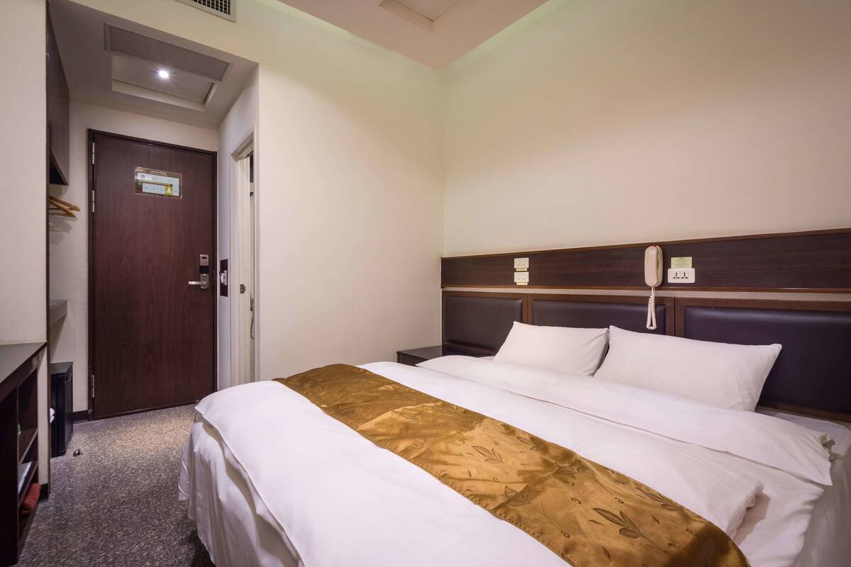 A hotel room with a bed, bedside table, and a wooden headboard.