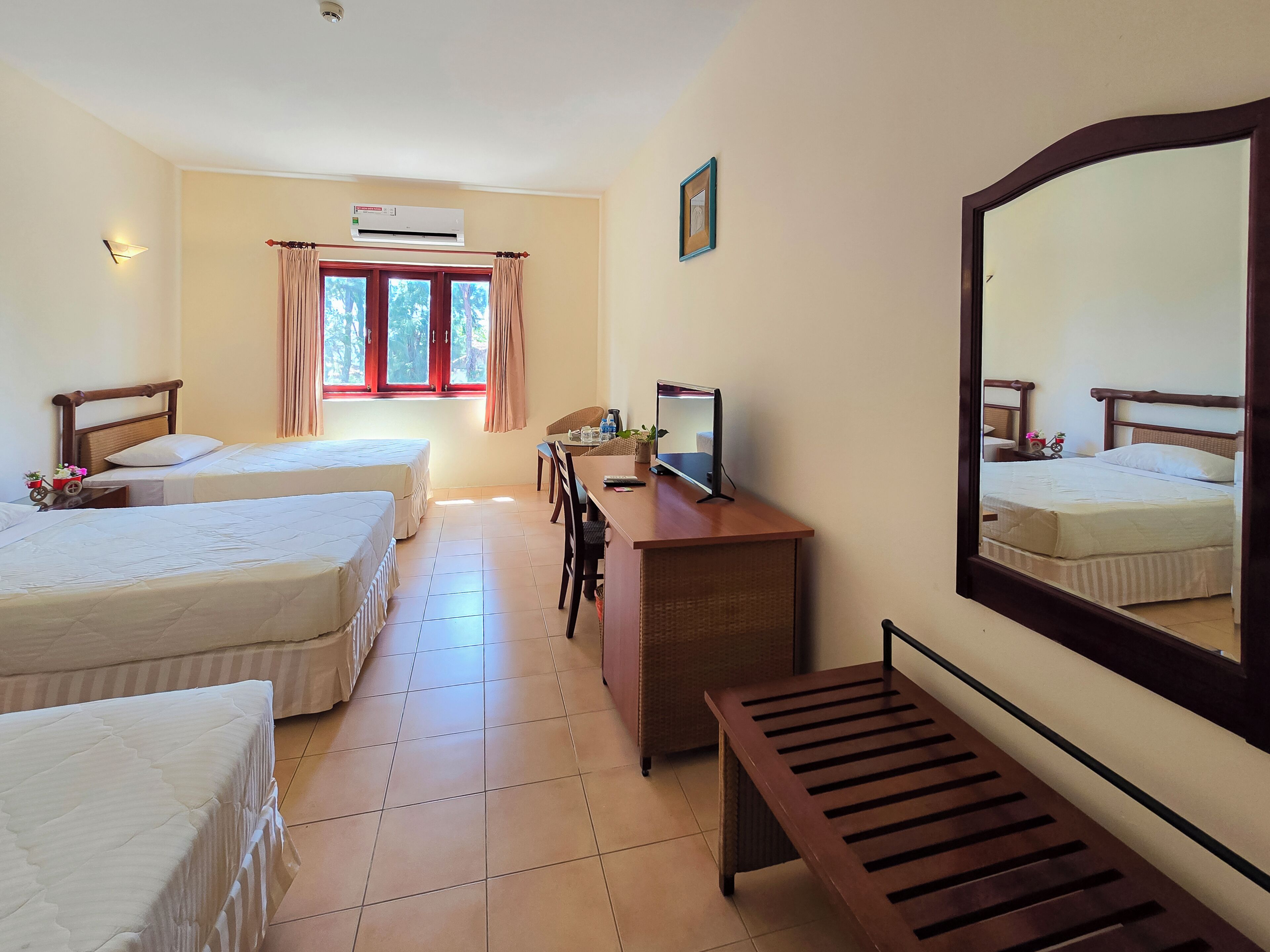 A hotel room with two beds, a desk with a computer, a mirror, and a window with curtains.